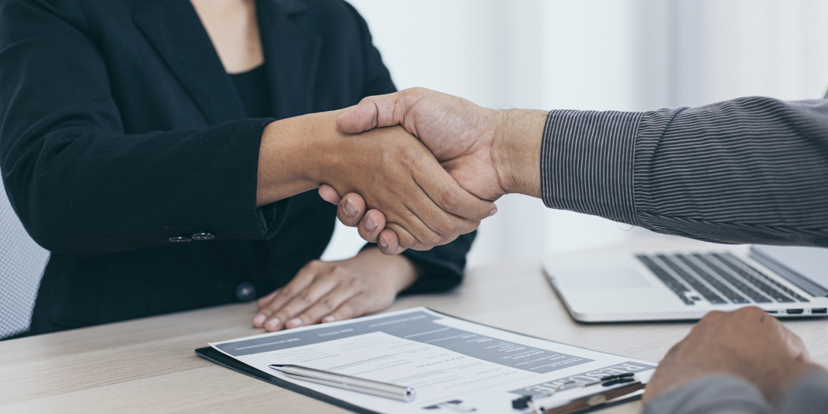 A man and a woman shaking hands over a table. Help writing selection criteria to land the job.